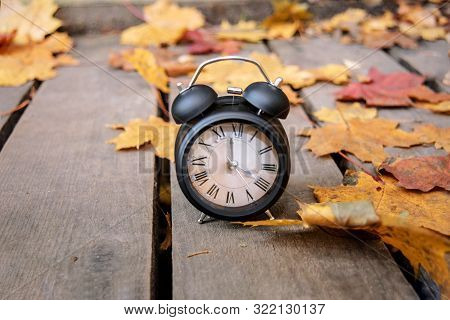 Vintage Black Alarm Clock On Autumn Leaves. Time Change Abstract Photo.