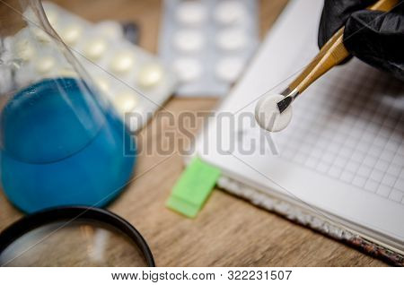 A Black Gloved Hand Holding A Pill With Tweezers Against A Background Of Reagent Pad. Illegal Pills,