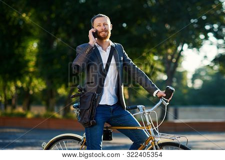 A Young Stylish Bearded Businessman In Suit Going To Work By Bike. Drinking Coffee From A Cup To Go 