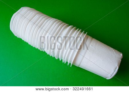 Stack of white plastic yogurt cups carefully prepared for recycling on green background. Separate waste collection concept.
