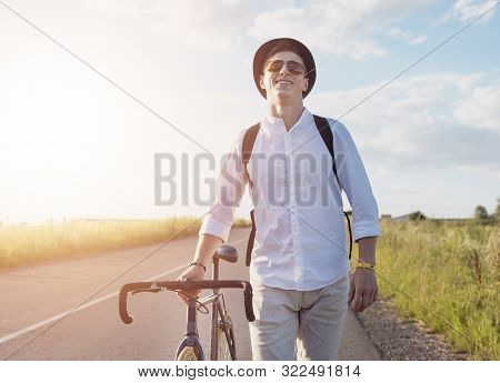 Young Male Cyclist Walking By Feet With A Grass Stalk In His Mouth On A Sunset Background
