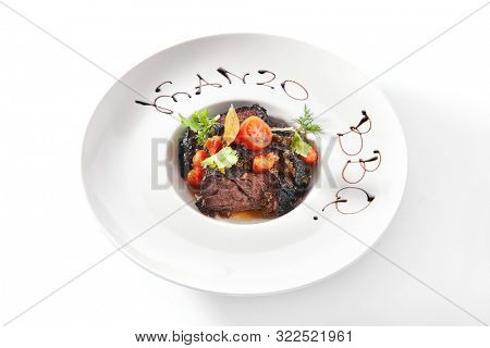Exquisite serving white restaurent plate of grilled prime beef with tomatoes, spices and herbs closeup. Restaurant main course with Well-done delicious veal meat, gourmet grillsteak isolated