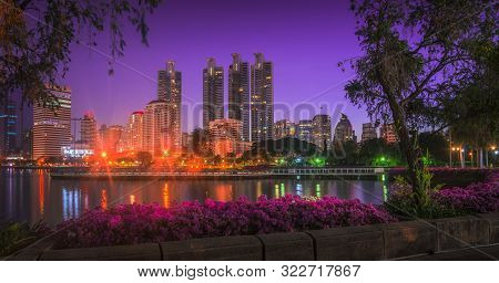 Lake In City Park Under Skyscrapers At Night. Benjakiti Park In Bangkok, Thailand