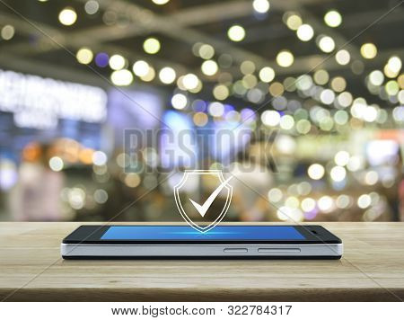 Security Shield With Check Mark Flat Icon On Modern Smart Mobile Phone Screen On Wooden Table Over B