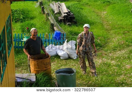 Smiling Old Man Yakut And A Young Asian Girl Fisherman With Gear Are In The Yard Of A Private House 