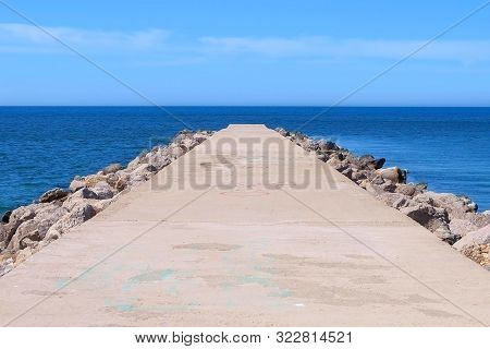 Seascape Background With Empty Long Stone Concrete Pier Stretching Out To Sea At Sunny Day. Cement P