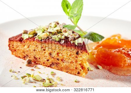 Healthy nut cake with apricot jam isolated on white background. Slice of walnut carrot sponge cake decorated with pistachios and fruit confiture on white round plate for restaurant menu