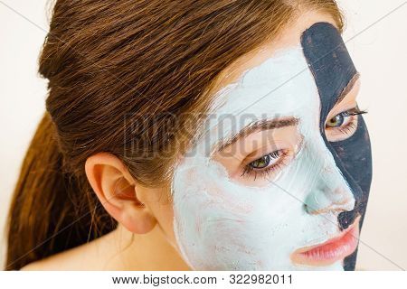 Woman With Clay Carbo Black Mask On Half Face And White Mud On Second Half. Girl Taking Care Of Oily