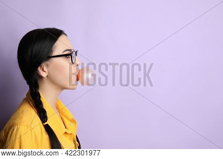 Fashionable Young Woman With Braids Blowing Bubblegum On Lilac Background, Space For Text