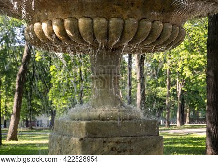 Fantan Close-up On The Background Of Green Trees Of The Park. Jets Of Water Flow Down From The Vase 