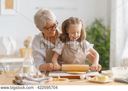 Happy loving family are preparing bakery together. Granny and child are cooking cookies and having fun in the kitchen. 