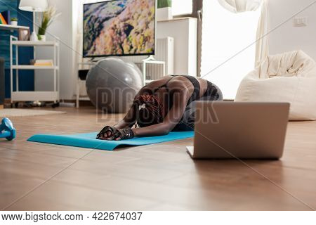 Black Woman Sitting On Yoga Mate Doing Stretching Relaxing Body After Watching Online Training Looki