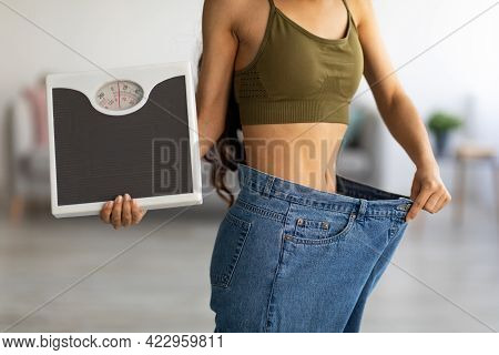 Closeup Of Indian Woman In Oversized Jeans Holding Scales, Showing Results Of Weight Loss Program Or