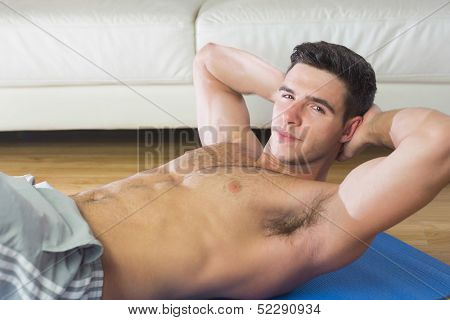 Handsome man doing sit ups in bright living room