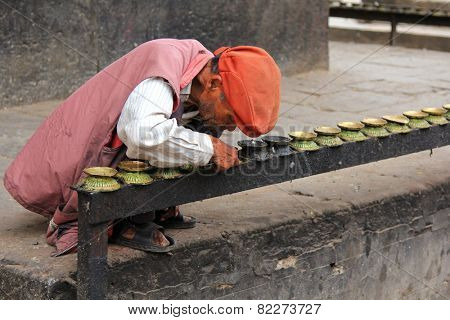 PATAN, NEPAL - APRIL 2014 : A Nepalese men removing soot from burning candle dishes at Kumbeshwar Temple on 13 April 2014 in Patan, Nepal. Kumbeshwar Temple is the oldest temple in Patan.