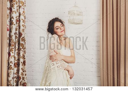Wedding dress fashion. Beautiful young bride in vintage crochet shawl, shabby chic champagne color wedding dress. Rustic wedding dress at model, in decorated interior, studio shot, high key.