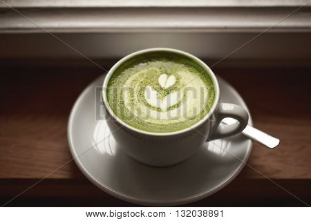Cup of green tea matcha latte with latte art, standing on wooden table.