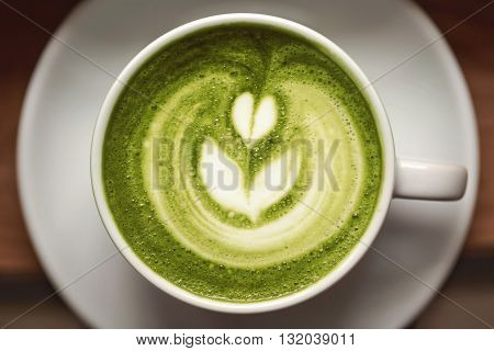 Cup of green tea matcha latte with latte art, standing on wooden table.