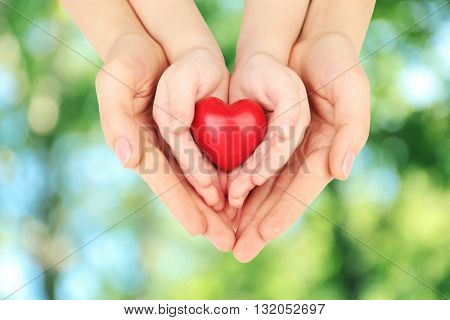 Heart in child and mother hands on green nature background. Concept of taking care, protection, helping and assistance