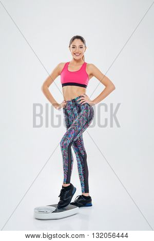 Full length protrait of smiling woman standing on weighing machine isolated on a white backgorund