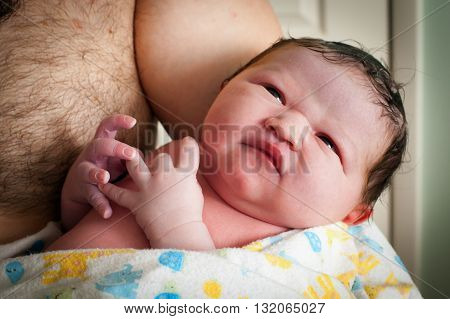 Close up of a newborn baby after a home birth. He is being held by his shirtless dad.