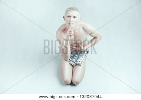 Male albino sits on the floor he covered his mouth with a finger showing quiet.