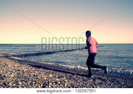 Tall Man In Dark Sportswer Running And Exercising On Stony Beach At Breakwater.