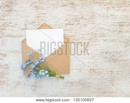 Brown paper envelope with white blank card and blue forget-me-not flowers bouquet tied with jute rope on the rustic white painted background