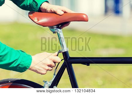 people, vehicle, eisure and lifestyle - close up of man adjusting fixed gear bike saddle high
