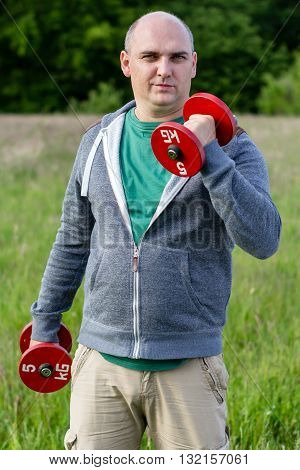 Man working outdoors with 5kg dumbbells. He holds one up.