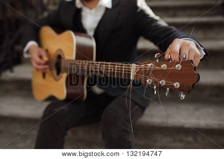 Young hipster playing guitar.  Close up of a man tuning his guitar.