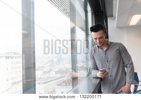relaxed young businessman using smart phone at modern startup business office meeting room  with big window and city in backgronud