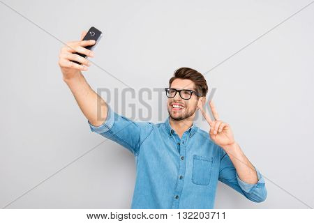Happy Man In Glasses Making Selfie On Smartphone And Showing Two Fingers