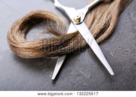Hairdresser's scissors with strand of brown hair on grey background
