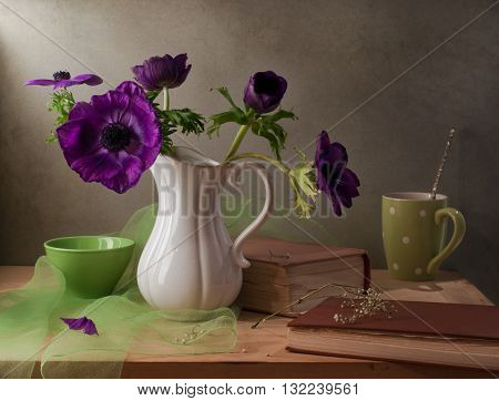 Still life with purple anemone flowers books and cup.