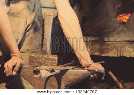 Blacksmith working metal with hammer on the anvil in the forge