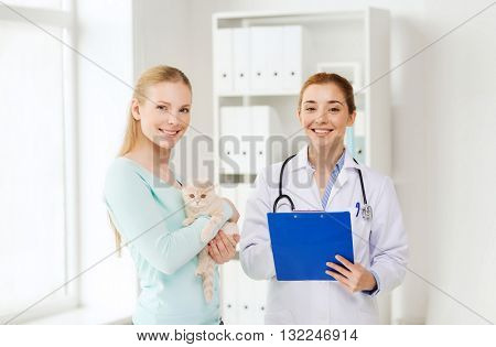 medicine, pet, animals, health care and people concept - happy woman holding scottish fold kitten and veterinarian doctor with clipboard at vet clinic