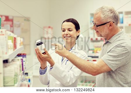 medicine, pharmaceutics, health care and people concept - happy pharmacist showing drug to senior man customer at drugstore