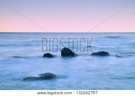 Romantic Morning At Sea. Big Boulders Sticking Out From Smooth Water Level. Pink Horozon With First