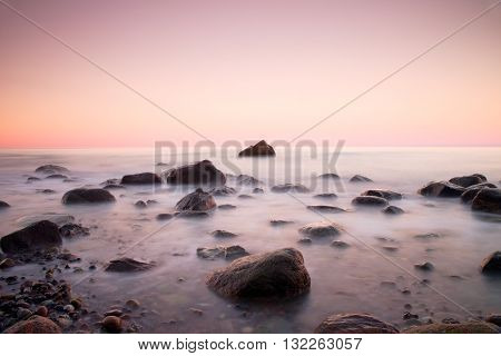 Sunset At Rocky Coast Of Sea. Low Shutter Speed For Smooth Water Level And Dreamy Effect