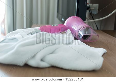 Pink hair dryer and white bath towel after used on wooden dressing table in hotel room.