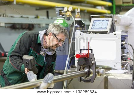 Industrial operator setting  computer controlled process of orbital welding machine in  stainless steel pipes manufacturing workshop.