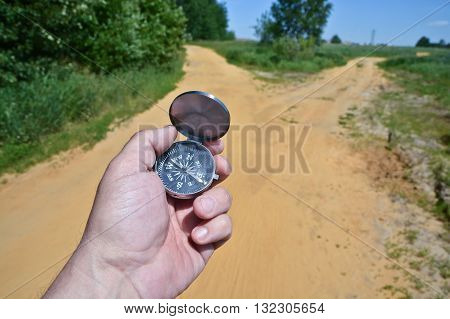 At the crossroads. Compass in the hand against the fork of the trail in the woods.