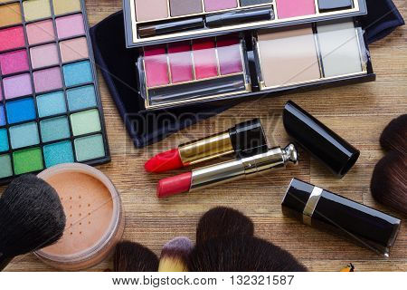 set of brushes, lipsticks, maskara, eye shadows and powder on wooden desktop