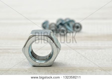 Big nut on wooden table with different crews on background. Tool of fastening. Fastener.  Parts for repair. Fixing bolts.
