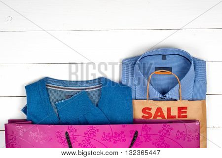 blue shirt and sweater for men with bags in the sales on wooden white background. Copy space for text.
