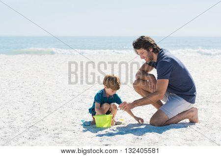 Father and son playing with toys at beach. Family of father and son enjoying summer vacation at beach. Father helping son fill basket with sand.