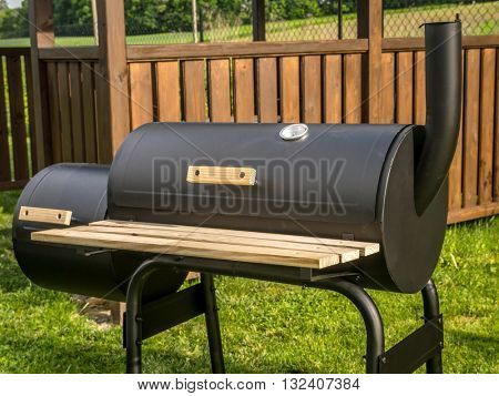 Black grill with chimney with wooden summer house in the background