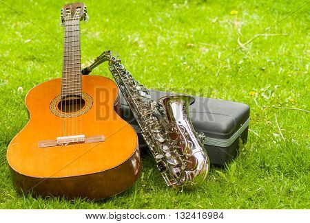 Beautiful golden saxophone and acoustic guitar lying across black instumental case on grassy surface.