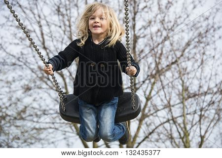 Little child blond girl having fun on a swing outdoor. Summer playground. Girl swinging high